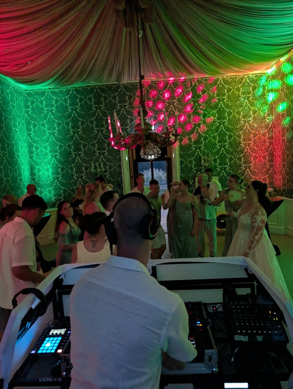 DJ Gluutje achter de draaitafel op een bruiloft met bruid en gasten onder groene en rode uplights